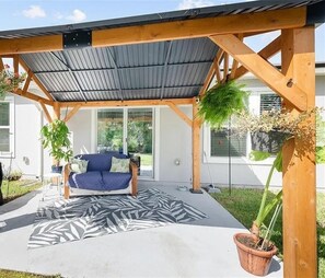Ein überdachter Patio-Bereich mit einem blauen Sofa, einem gemusterten Teppich und Topfpflanzen.