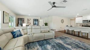 Ein Wohnzimmer mit einer Couch, einem Deckenventilator und einer Küchenzeile mit Mikrowelle und Barhocker.