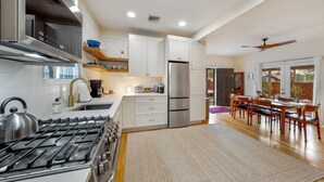 Una cocina moderna con estufa a gas, electrodomésticos de acero inoxidable, armarios blancos y un comedor con mobiliario de madera.