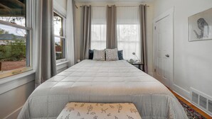 Un dormitorio con una cama grande, una mesita de noche, una ventana con cortinas y un cuadro colgado en la pared.
