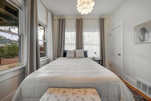 Ein Schlafzimmer mit einem großen Bett, einem Nachttisch, einem Fenster mit Vorhängen und einem Wandbild.