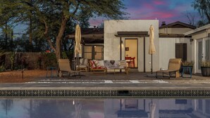 Un área junto a la piscina con mobiliario exterior, un porche cubierto y vistas de la casa.