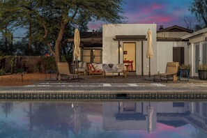Ein Poolbereich mit Gartenmöbeln, einer überdachten Terrasse und Blick auf das Haus.