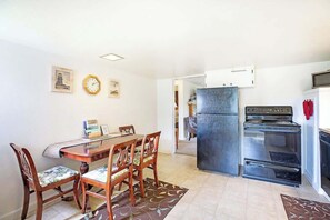 Eine kleine Küche mit Kühlschrank, Backofen und Esstisch mit Stühlen.
