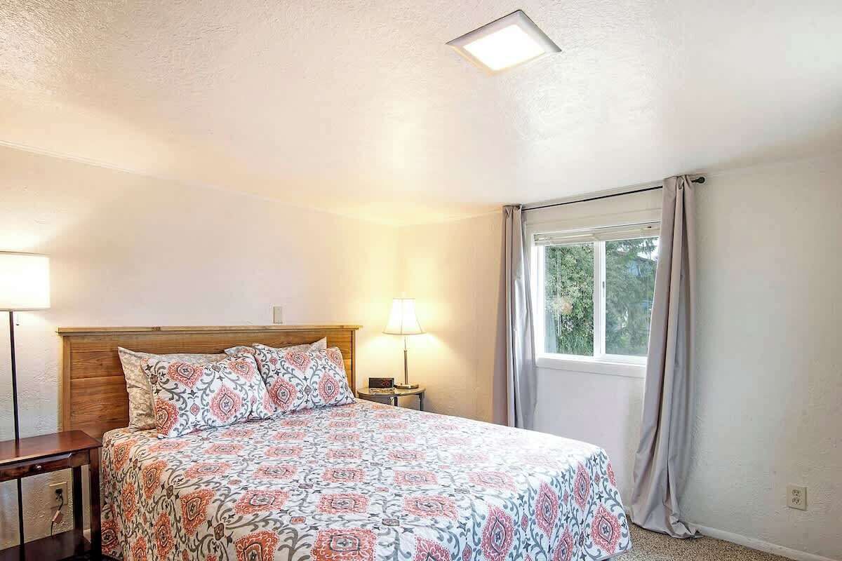 A bedroom with a bed, bedside lamps, a window with curtains, and a ceiling light.