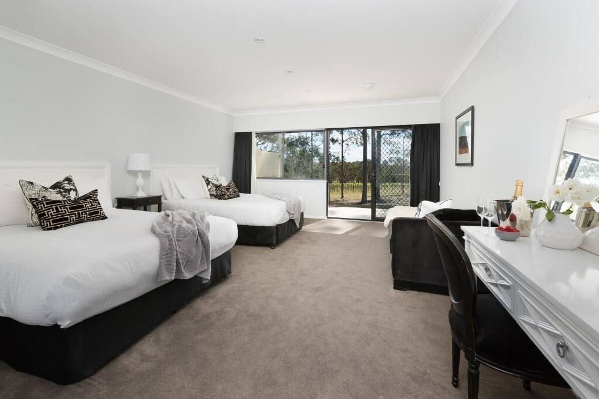 A hotel room with two beds, a desk, and a large sliding glass door leading to an outdoor area.