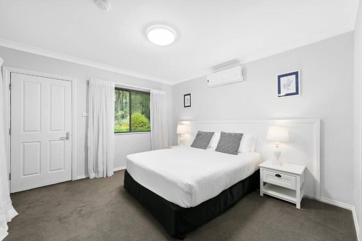 A bedroom with a bed, bedside tables, a window with curtains, and a door.