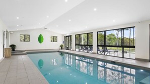 An indoor swimming pool with clear glass walls, a tiled floor, and a ceiling with recessed lighting. - Nu Leaf Retreat (Pokolbin)