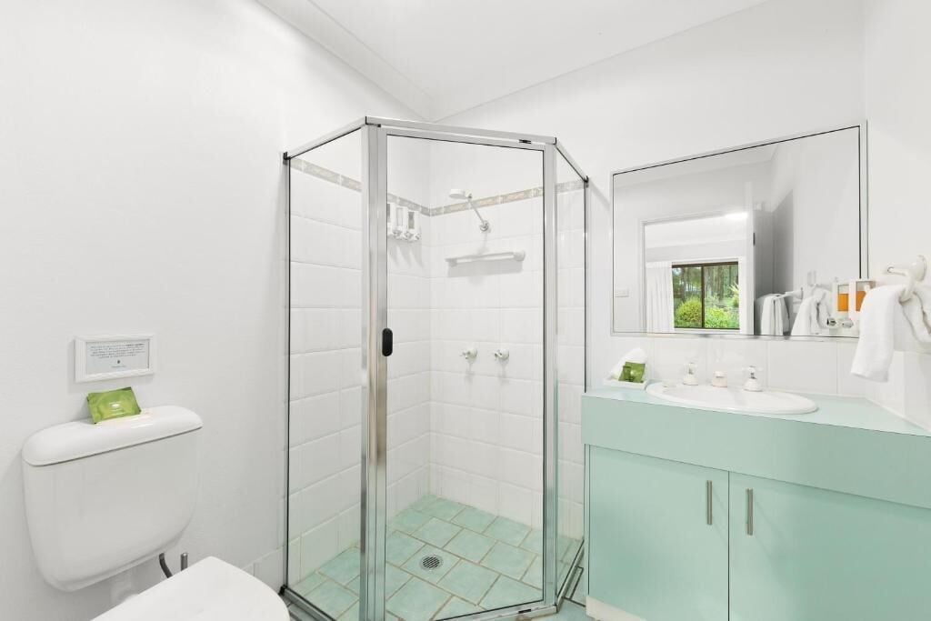 Een badkamer met een douchecabine van glas, een wit toilet, een wastafel met spiegel en een kast.