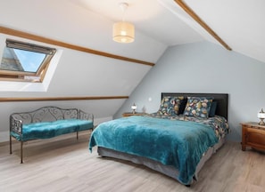 Ein Schlafzimmer mit Oberlicht, einem Bett mit floralem Bettbezug, einer Bank und einem Nachttisch mit Lampe.