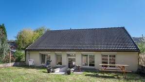 Ett enplanshus med ett tak täckt med takpannor, en veranda och en liten uteplats med utemöbler.