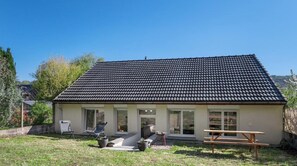 Einbungalow mit Ziegeldach, einer Veranda und einer kleinen Terrasse mit Sitzgelegenheit.