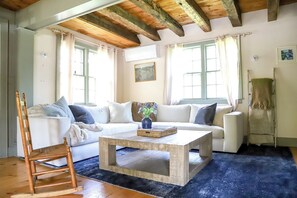 A living room with a white sofa, a wooden rocking chair, a coffee table, and a blue rug. - Quintessential 4-bedroom farmhouse with AC in Kennebunkport (Kennebunkport)