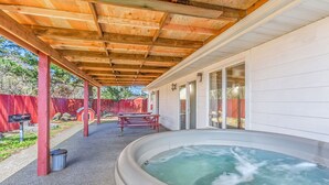 Ett takförsett utomhusområde med en bubbelpool, picknickbord och ett rött staket.