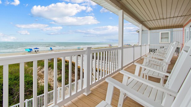 A covered deck with white railings and wooden flooring, overlooking a beach with umbrellas and lounge chairs. - "Heavenly View" 5 Bedroom, 4 Bathroom, Oceanfront with Private Pool PET FRIENDLY! (Holden Beach)