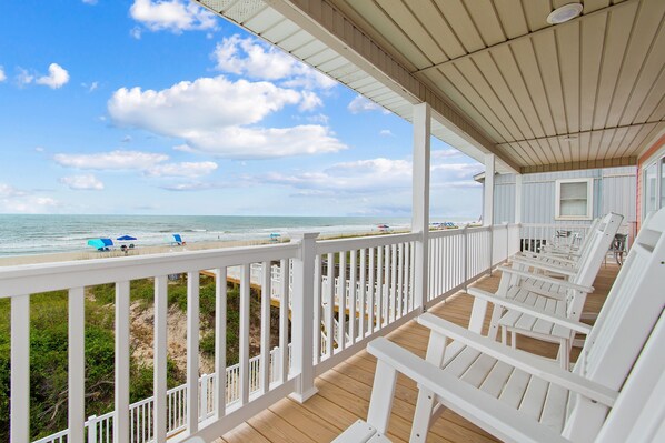 A covered deck with white railings and wooden flooring, overlooking a beach with umbrellas and lounge chairs. - "Heavenly View" 5 Bedroom, 4 Bathroom, Oceanfront with Private Pool PET FRIENDLY! (Holden Beach)
