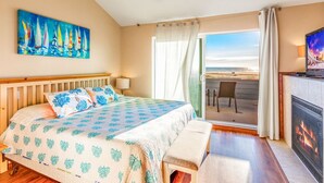 A bedroom with a bed, a bench, a fireplace, a painting, a ceiling fan, and a view of the beach. - Beachfront w/ Hot Tub | Sleeps 11 | Dogs OK (Ocean Shores)