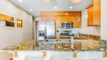 A kitchen with wooden cabinets, stainless steel appliances, a granite countertop, and pendant lighting.