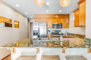 A kitchen with wooden cabinets, stainless steel appliances, a granite countertop, and pendant lighting.