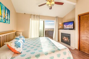 A bedroom with a bed, a television, a fireplace, and a view of the ocean.