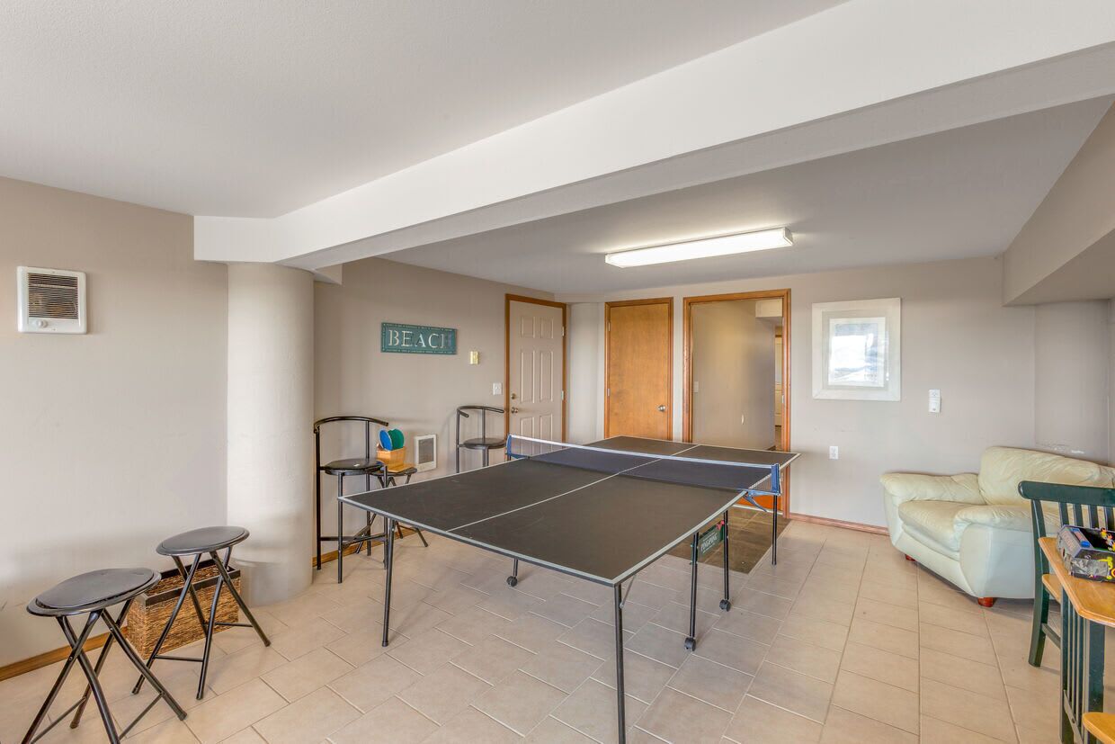 A room with a ping pong table, chairs, a sofa, and a door labeled 'BEACHT'.