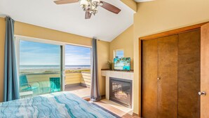 A bedroom with a large bed, a fireplace, a sliding glass door to a balcony, and a ceiling fan. - Beachfront Home w/ Hot Tub | Sleeps 9 | Dogs OK (Ocean Shores)