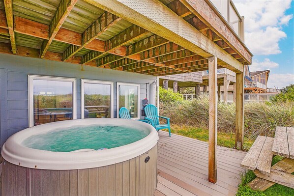 Un jacuzzi en una terraza de madera con sillas, un porche cubierto y vistas a una casa.