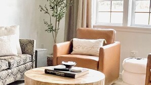 A living room with a round wooden coffee table, a sofa, a chair, and a potted plant.