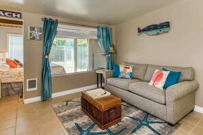 Un salon comprenant un canapé, une petite table, une décoration murale en forme d’étoile de mer et une fenêtre avec des rideaux.