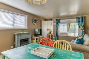 A living room with a fireplace, television, and a table with a tray. - Beachfront Condo | Walk to DT | Dogs OK | Unit A (Ocean Shores)
