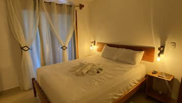 Un letto rifatto con un'ossatura in legno, un comodino con una lampada e una finestra con tende.