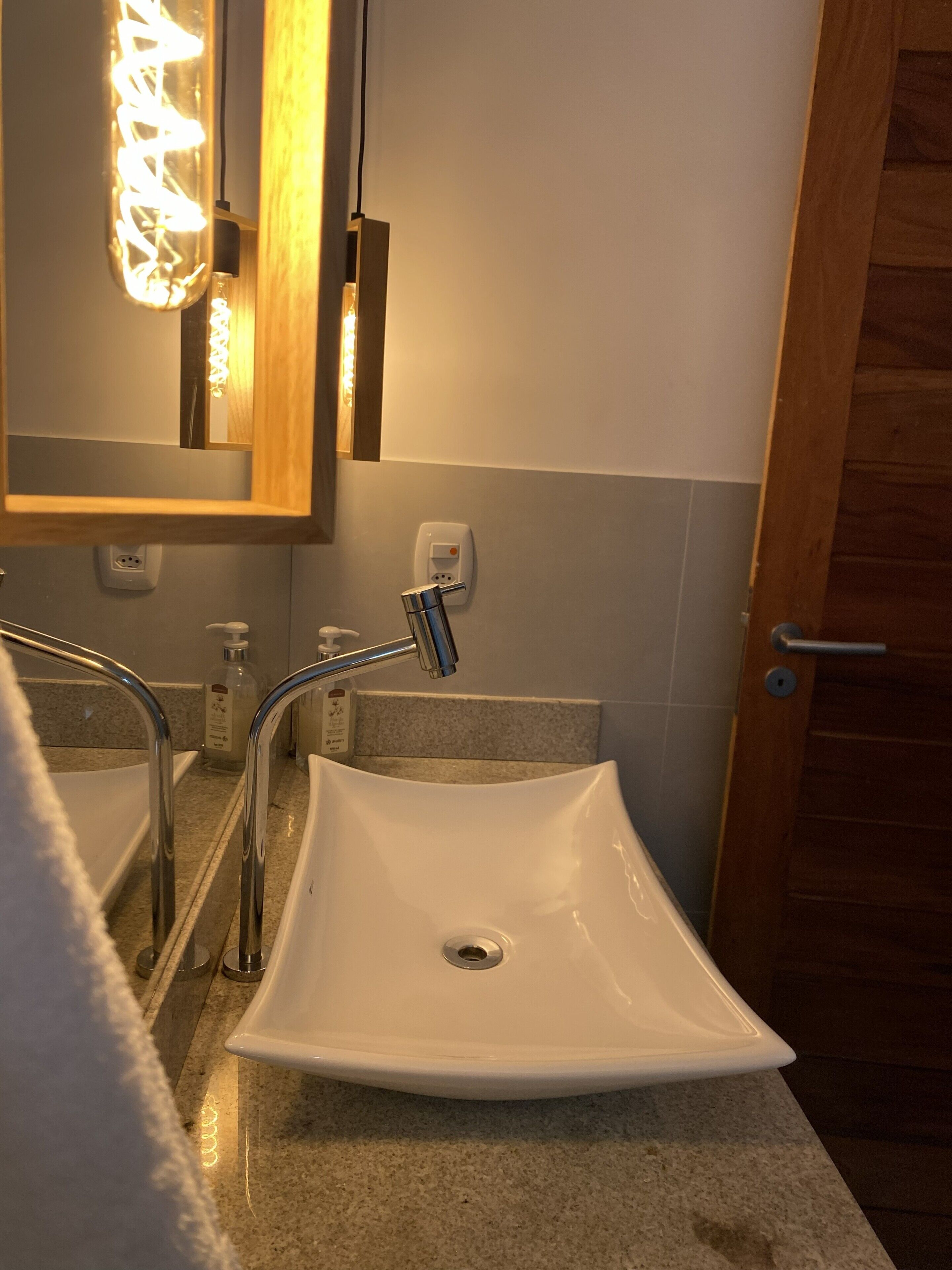 Un bagno con un lavandino bianco, uno specchio, un asciugamano e una porta in legno.