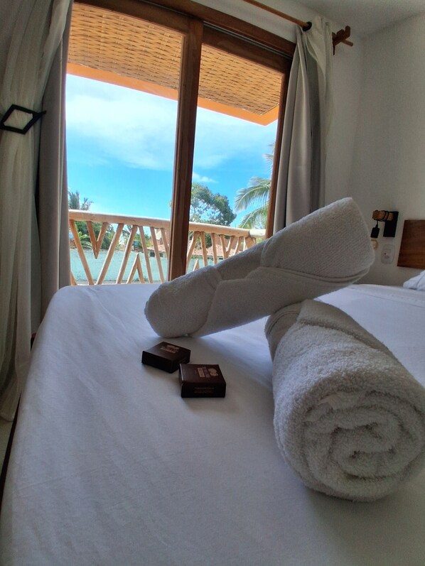 Habitación de hotel con cama, vista al océano y balcón con barandillas de madera.