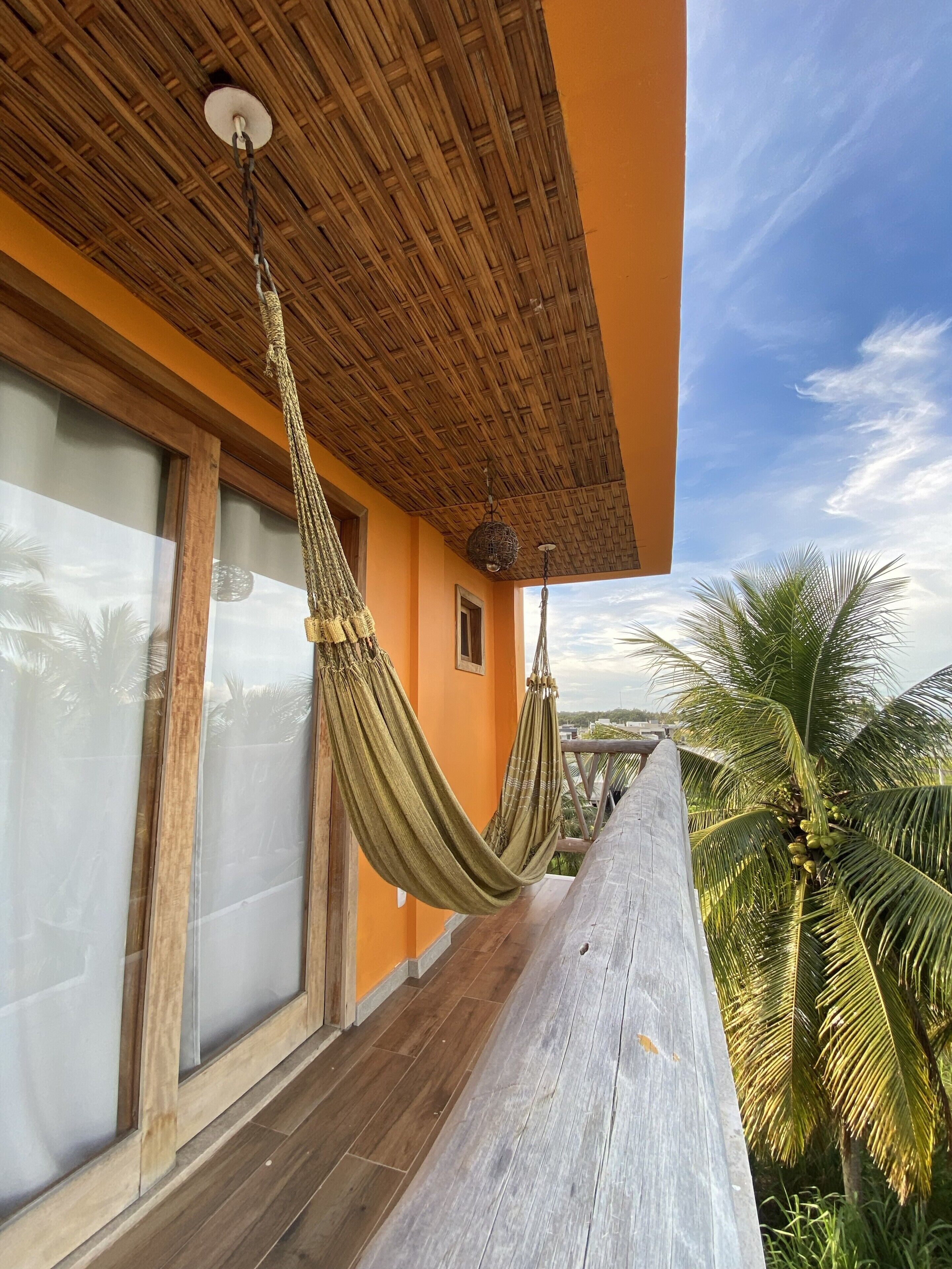 Ein Balkon mit Holzboden, einer gewebten Hängematte und Blick auf Palmen.