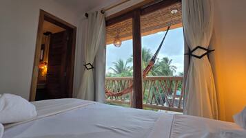 A hotel room with a bed, curtains, a view of palm trees, and a hammock.