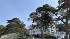 Ein mehrstöckiges Gebäude mit weißer Fassade und blauen Balkonen, umgeben von üppiger Vegetation und Bäumen.