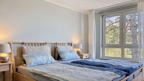Ein Schlafzimmer mit einem Bett, zwei Nachttischen, einem Fenster und Blick auf Bäume.