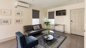 A modern living room with a sofa, a coffee table, and a TV mounted on the wall. - The Blue Heron-elegant urban studio in city center (Memphis)