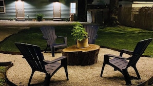 Een achtertuin met een houten tafel, vier Adirondack-stoelen en een bloempot.