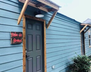 Un bâtiment bleu avec une porte sombre, une pergola en bois et un panneau lumineux au néon sur lequel on peut lire « Boo Groove ».