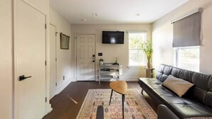 Een woonkamer met een bank, een salontafel, een televisie en een raam met zonwering.