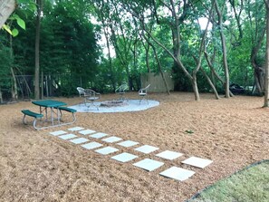 Een achtertuin met een picknicktafel, terrasstoelen, een vuurkorf en een pad van stenen.