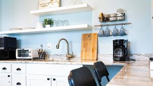 A kitchen with a microwave, toaster, sink, coffee maker, and a wooden cutting board.