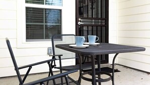 A small outdoor table with two chairs, a door with a decorative handle, and a window with blinds.
