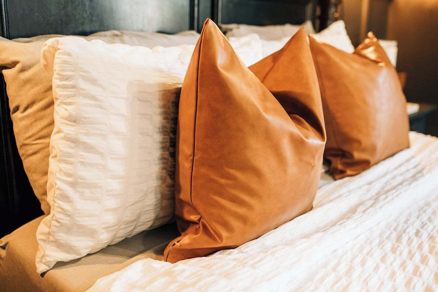 Een bed met witte en bruine kussens, een witte sprei en een donker hoofdbord.