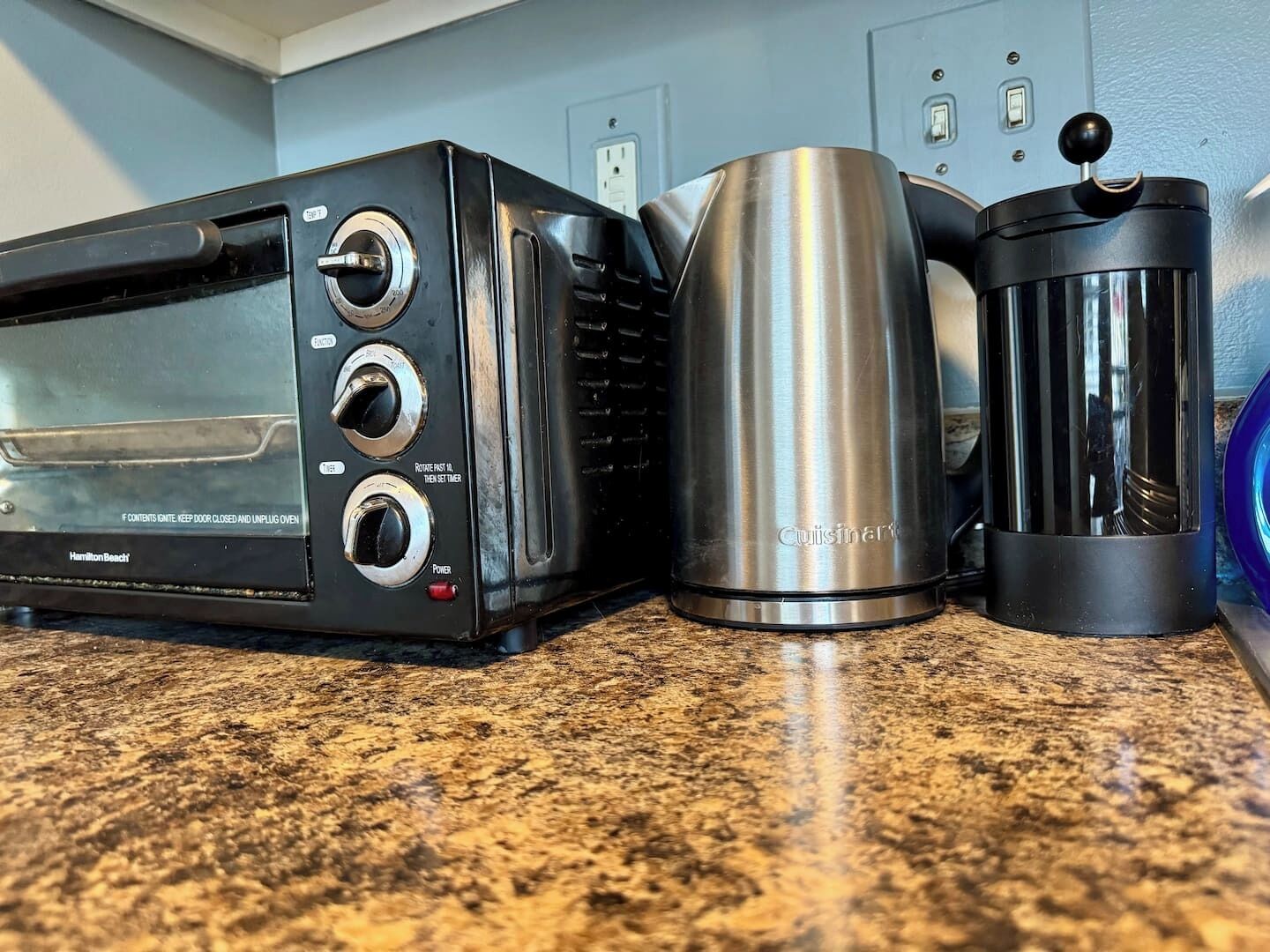 Una cocina con un tostador, un recipiente de acero inoxidable y una cafetera sobre una encimera de granito.