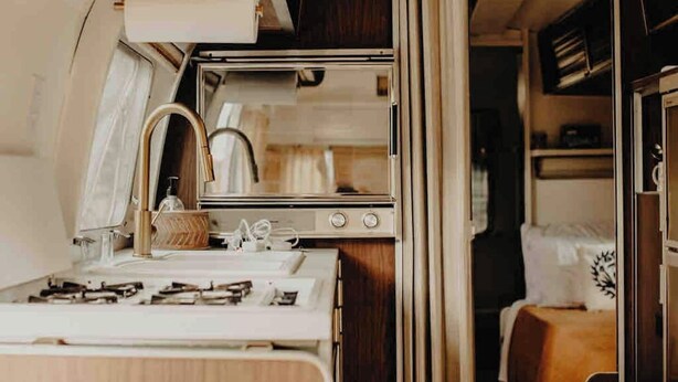 Una kitchenette compacta con estufa, lavamanos y espejo.