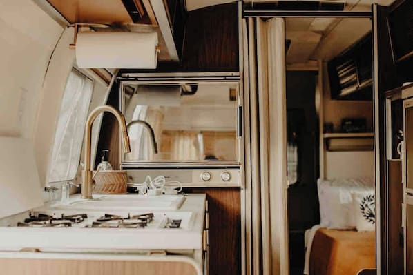 Una kitchenette compacta con estufa, lavamanos y espejo.