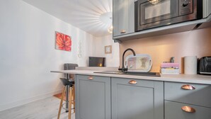 Uma cozinha moderna com armários cinzentos, um micro-ondas de aço inoxidável, uma pia e um banco de bar.