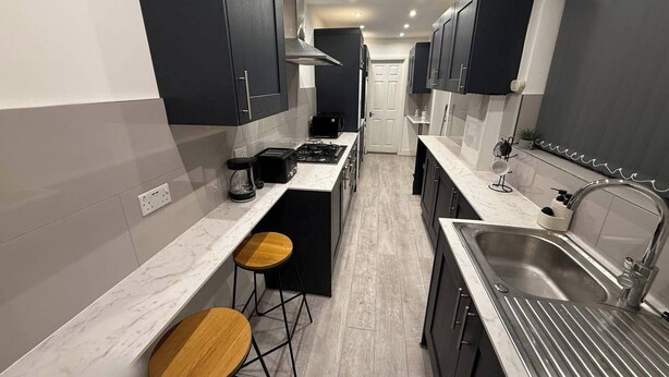 Una cocina moderna con armarios oscuros, una isla central, taburetes de bar y un lavamanos de acero inoxidable.